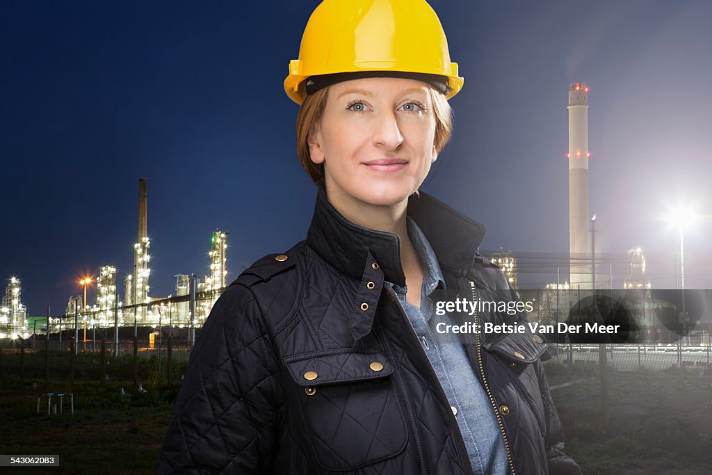 Female engineer stands in front of oil refinery.