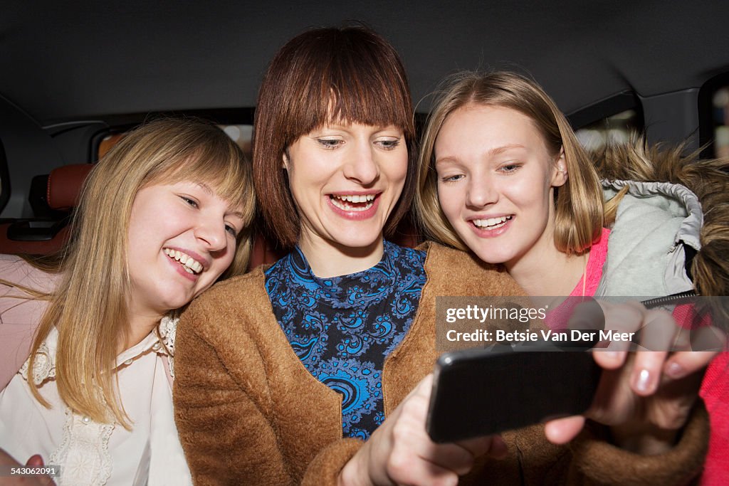 Three sisterstaking Selfie in cab at night.