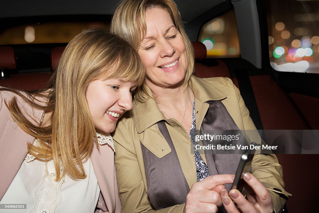 Mother and daughter looking at phone in backseats.