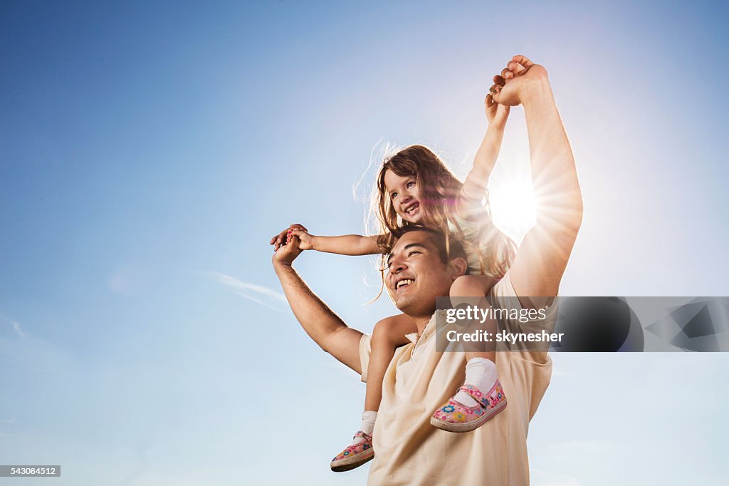 Père fille asiatique transportant sur les épaules contre le ciel bleu.