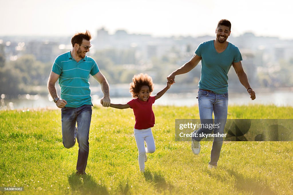 Two happy men running with African American little girl outdoors.
