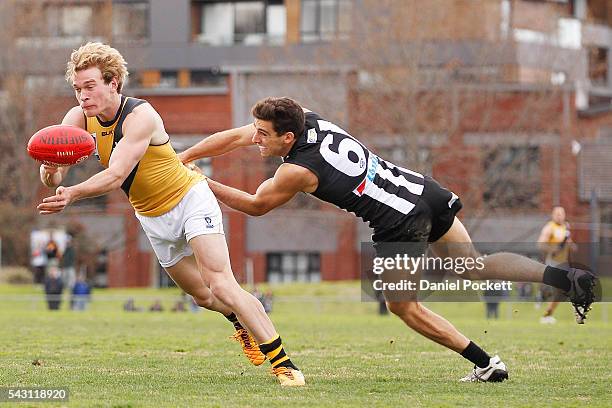 Nick Mellington of the Tigers handballs whilst being tackled by Nick Gray of the Magpies during the round 12 VFL match between the Collingwood...