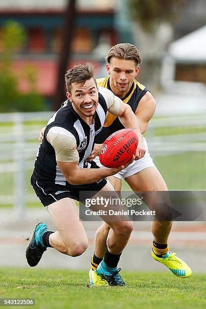 Matthew Smith of the Magpies handballs whilst being tackled by Dan Butler of the Tigers during the round 12 VFL match between the Collingwood Magpies...