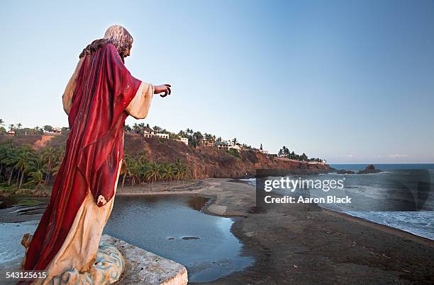 statue of jesus wearing red cloak overlooks a beach and small town. - michoacán state stock pictures, royalty-free photos & images