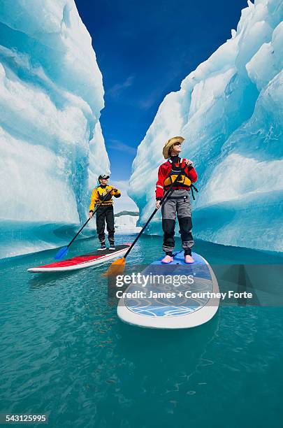 a couple on stand up paddle boards (sup) explore an iceberg canyon on bear lake in kenai fjords national park, alaska. - iceberg stock photos et images de collection