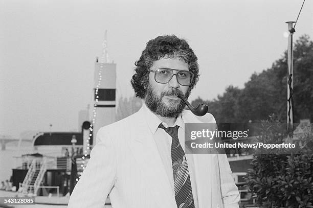 English DJ and radio broadcaster, Dave Lee Travis pictured smoking a pipe beside the River Thames in London on 5th August 1982.