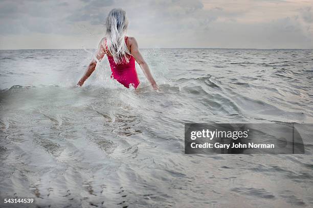 senior woman standing in the ocean waves. - swimming costume stock pictures, royalty-free photos & images