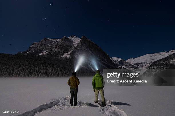 couple stand in snowy mtn clearing, with headlamps - weggucken stock-fotos und bilder