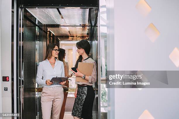 caucasian businesswomen talking in elevator - elevator fotografías e imágenes de stock