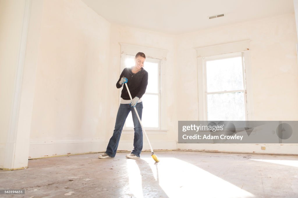Mixed race woman sweeping floor of new home