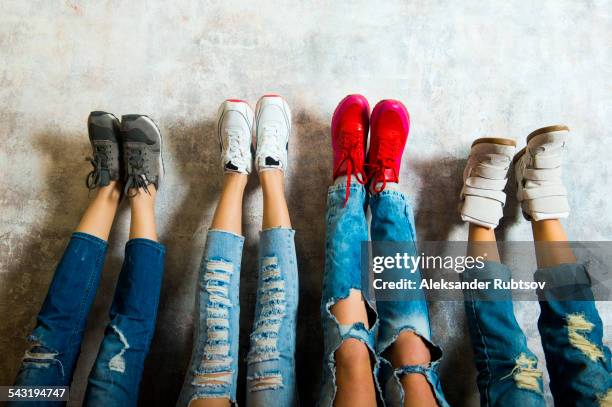 caucasian women admiring their sneakers against wall - zerrissene jeans stock-fotos und bilder