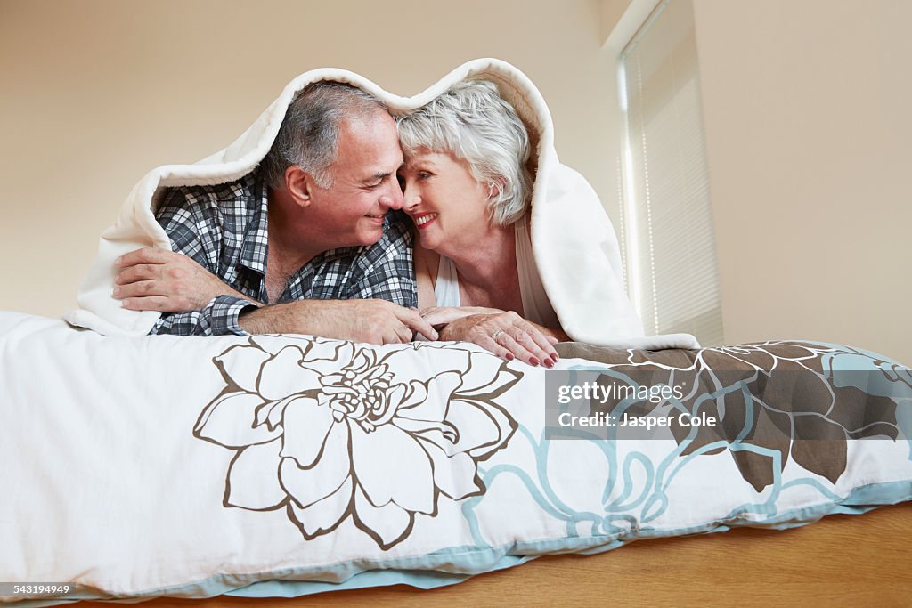 Older couple rubbing noses under blanket on bed