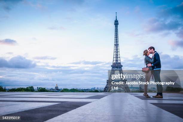 caucasian couple kissing near eiffel tower, paris, france - champs de mars stockfoto's en -beelden