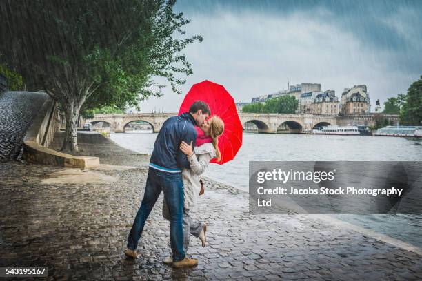 caucasian couple kissing under heart shape umbrella - rain kiss stock pictures, royalty-free photos & images