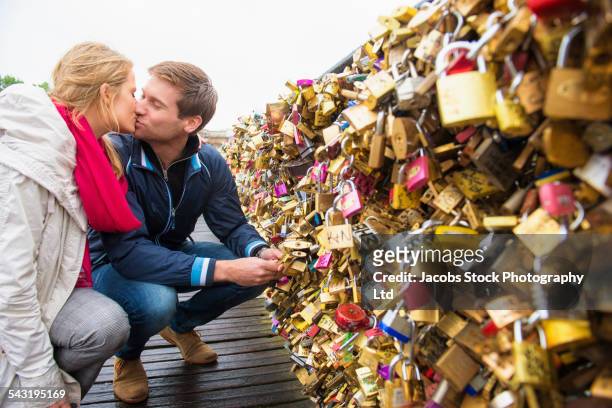 kissing caucasian couple locking padlock to bridge, paris, france - pont des arts padlocks stock pictures, royalty-free photos & images