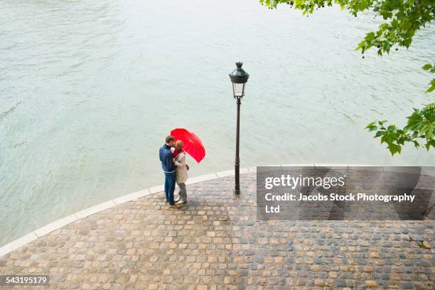 caucasian couple kissing under heart shape umbrella - escapade urbaine photos et images de collection