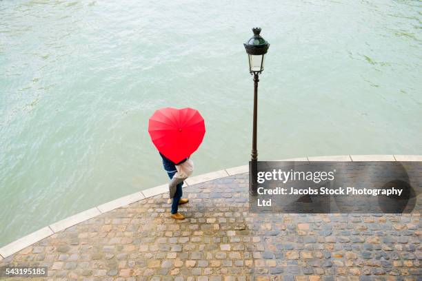 caucasian man lifting girlfriend under heart shape umbrella - intertwined stock-fotos und bilder