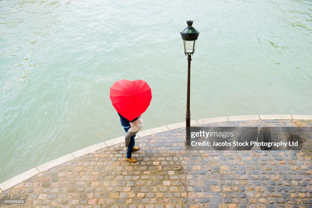 Caucasian man lifting girlfriend under heart shape umbrella