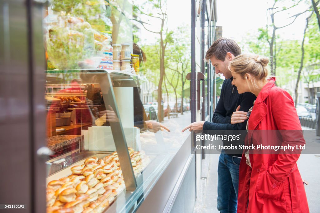 Caucasian couple admiring pastries in bakery window