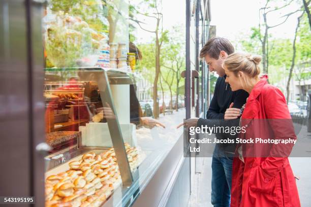 caucasian couple admiring pastries in bakery window - boulangerie paris stock pictures, royalty-free photos & images