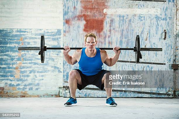 caucasian man lifting weights in warehouse - hombre agachado fotografías e imágenes de stock