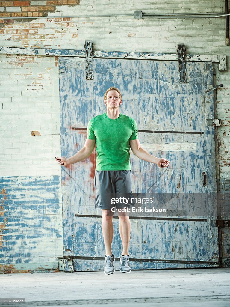 Caucasian man jumping rope in warehouse