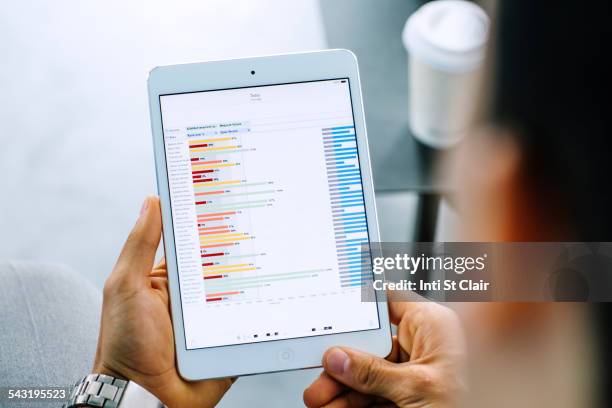 mixed race businessman examining graph on digital tablet - ipad halten stock-fotos und bilder