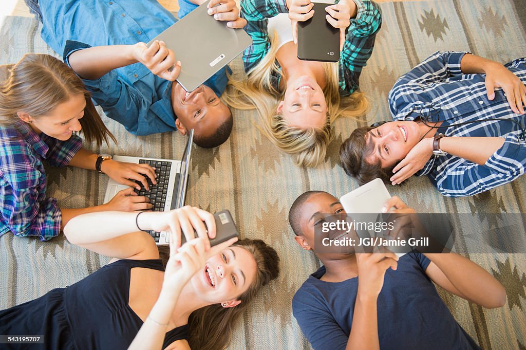 Teenagers laying on floor using technology