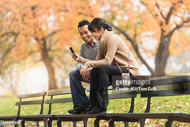 couple using cell phone on park bench - couple central park stockfoto's en -beelden