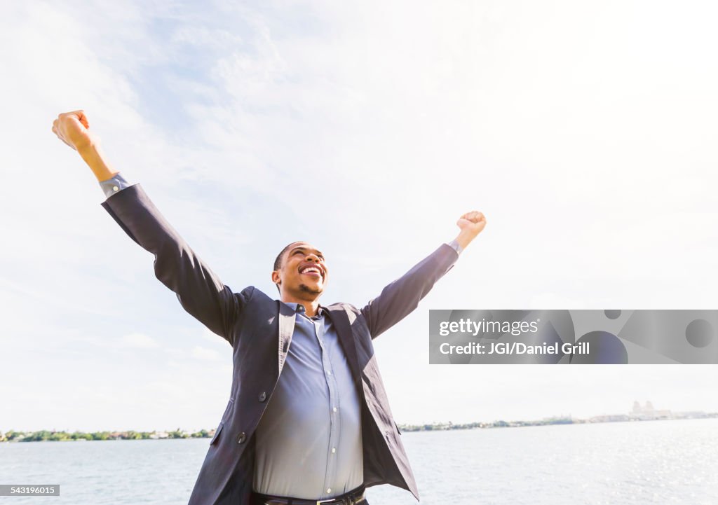 Black businessman cheering with arms outstretched outdoors