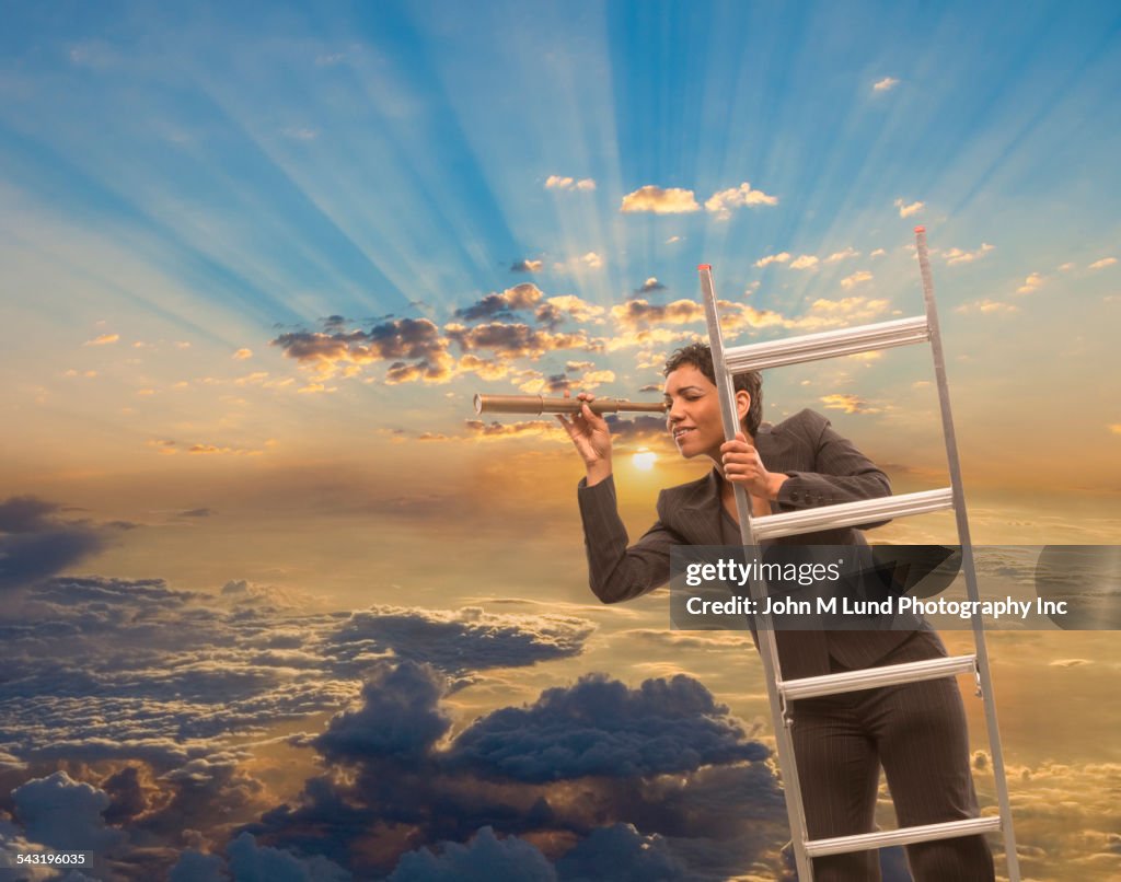 Mixed race businesswoman using telescope on ladder above clouds