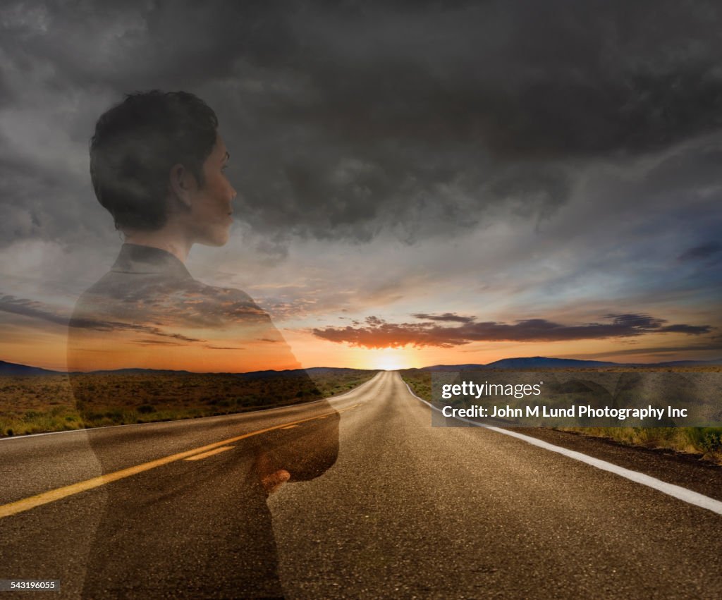 Mixed race businesswoman on remote road under sunset sky