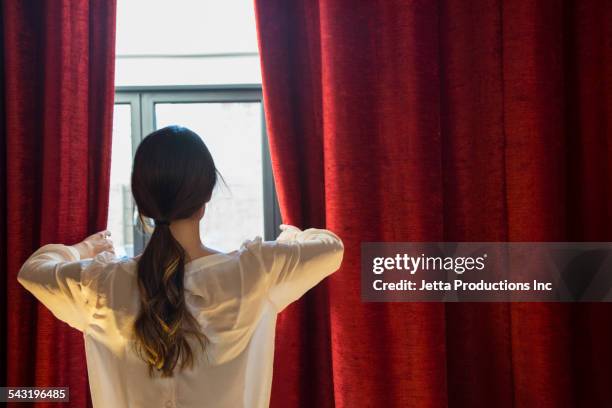 mixed race woman opening curtains - red curtain stock-fotos und bilder