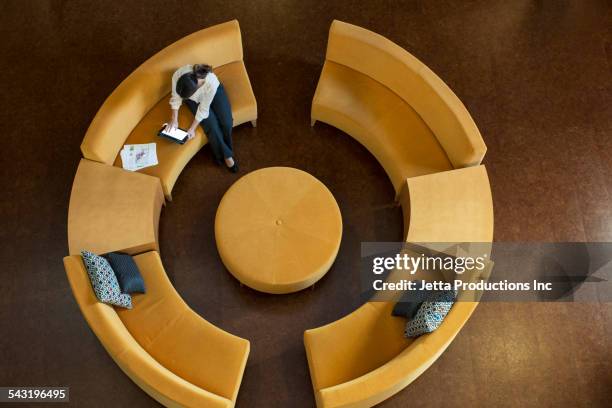 mixed race businesswoman using digital tablet on circular sofa - office elevated view stock pictures, royalty-free photos & images