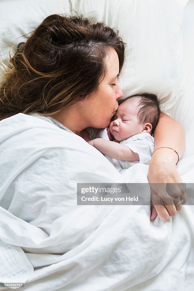 High angle view of mother kissing baby in bed