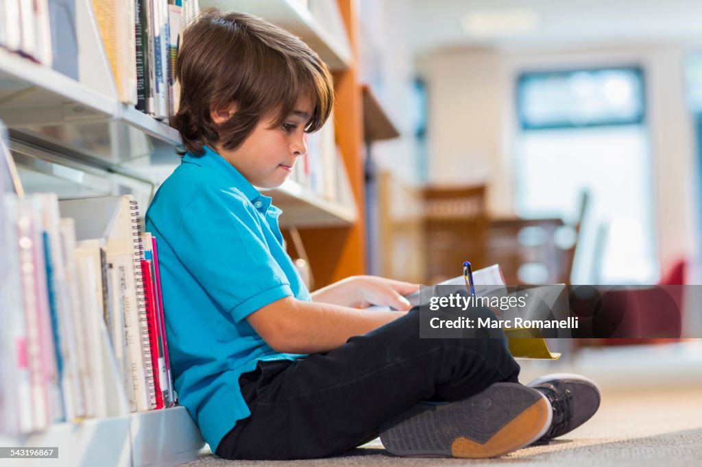 Mixed race student writing in notepad on floor in library