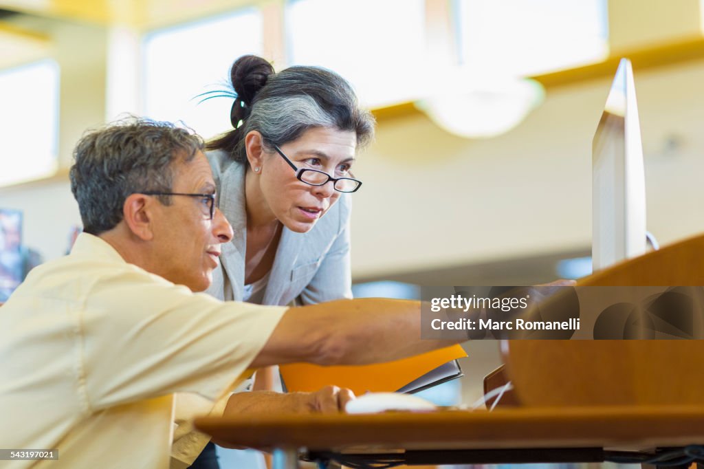 Teacher helping adult student use computer in library