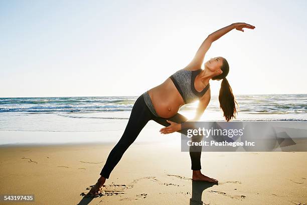 Pregnant Hispanic woman practicing yoga on beach