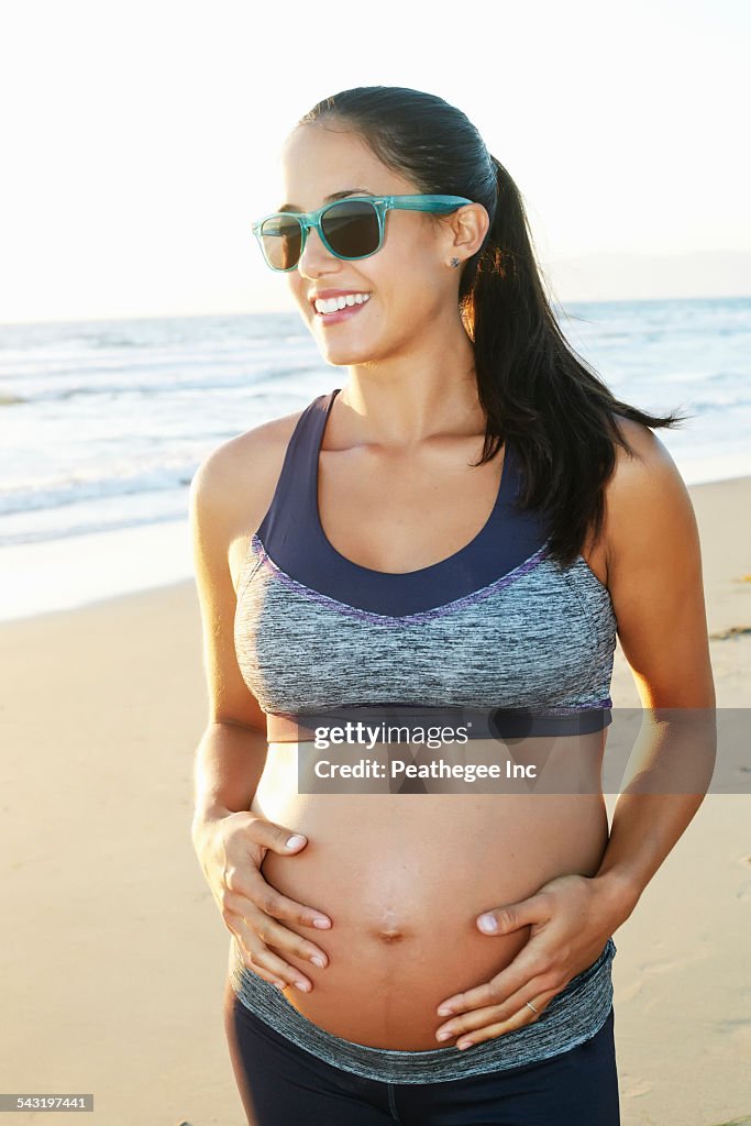 Pregnant Hispanic woman holding her stomach on beach