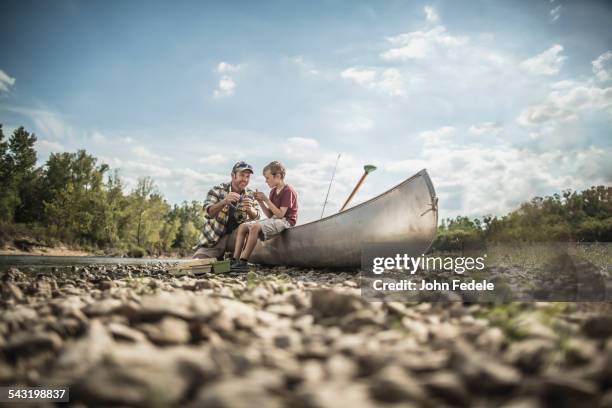 caucasian father and son sitting in canoe on riverbed - riverbed fotografías e imágenes de stock