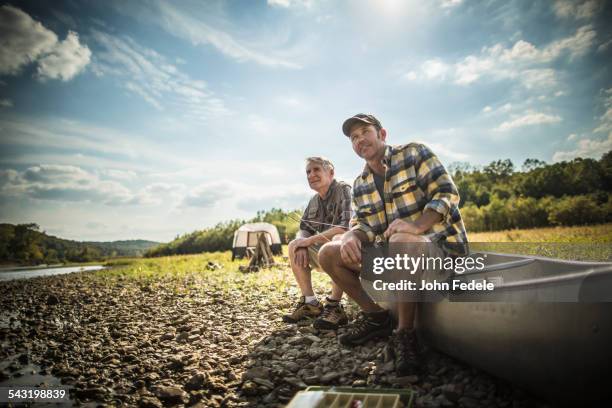 caucasian father and son sitting in canoe on riverbed - active seniors outdoors stock-fotos und bilder