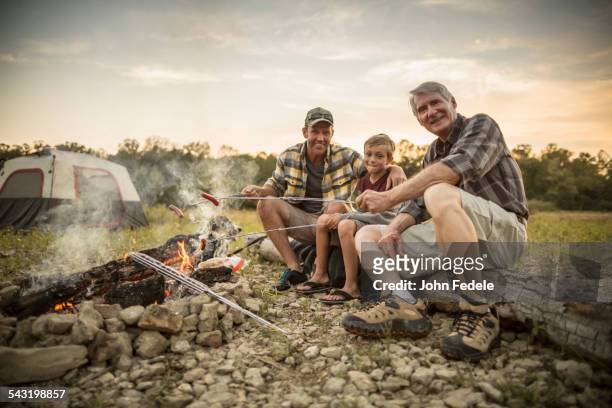 three generations of caucasian men roasting hot dogs over campfire - missouri mittlerer westen stock-fotos und bilder