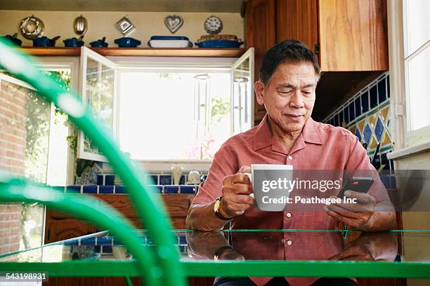 filipino man using cell phone in kitchen - senior men coffee stock pictures, royalty-free photos & images