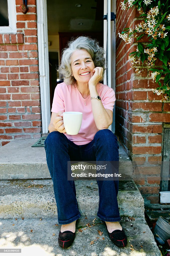 Caucasian woman drinking cup of coffee on front stoop