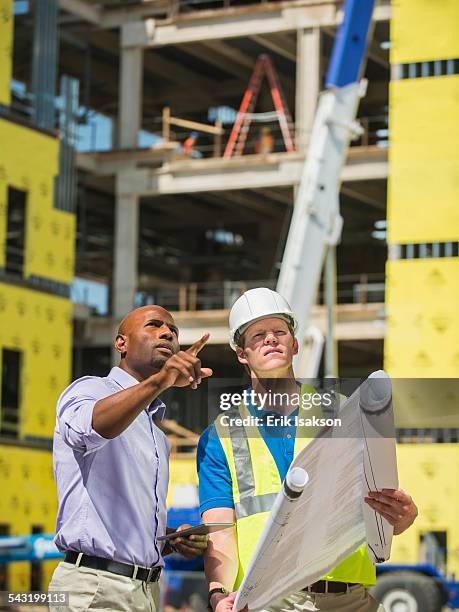 businessman and construction worker reading blueprints at construction site - business man overseeing blueprints outdoor stock-fotos und bilder