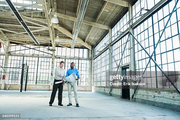 businessmen reading blueprints in empty warehouse - commercieel vastgoed stockfoto's en -beelden