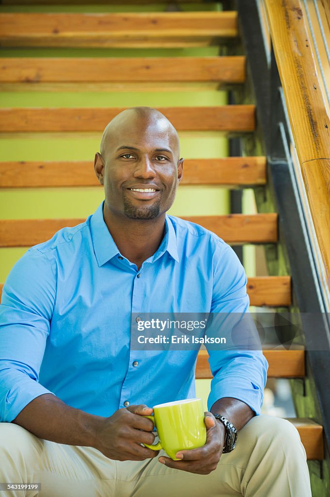Black businessman drinking cup of coffee on staircase