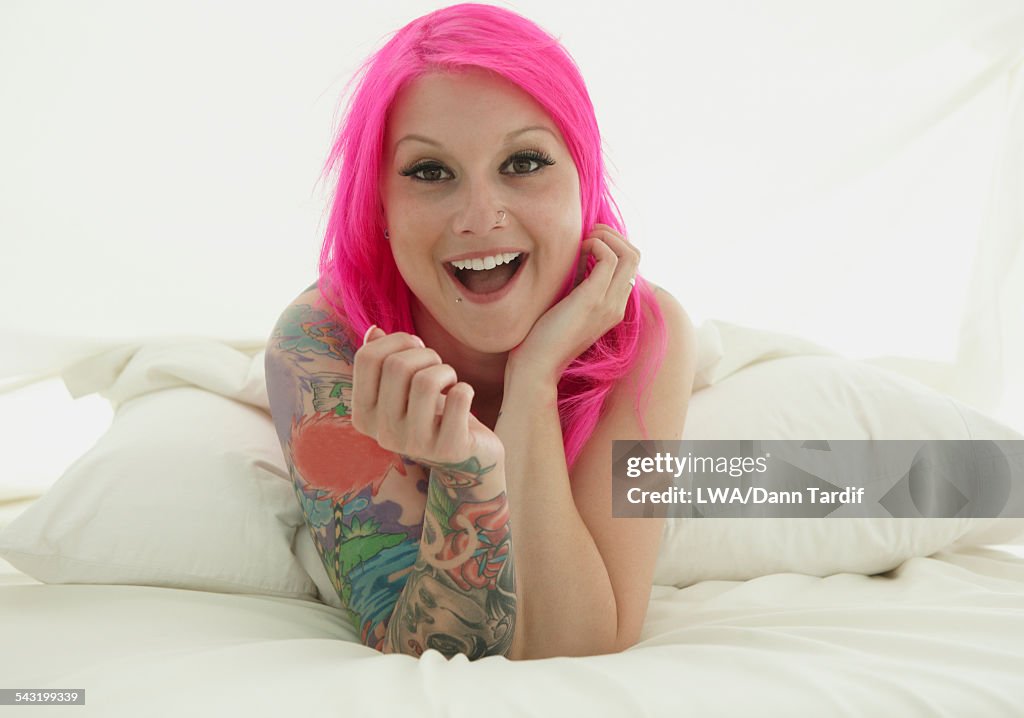 Caucasian woman with pink hair and tattoos laying on bed