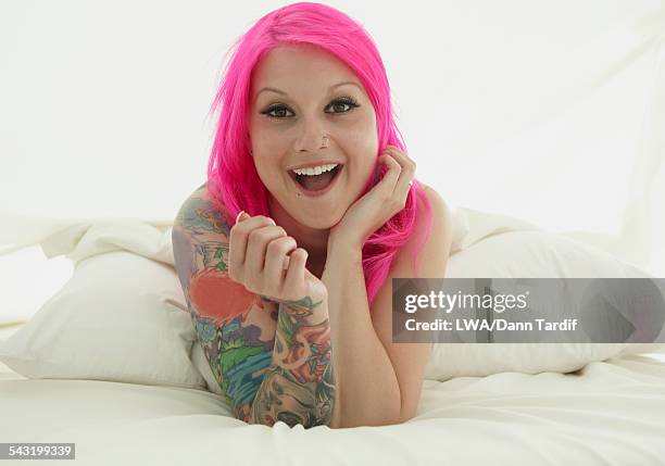 Caucasian Woman With Pink Hair And Tattoos Laying On Bed High-Res Stock Photo