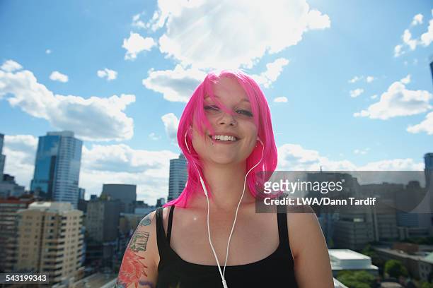 caucasian woman with pink hair and tattoos listening to earbuds in city - walkman closeup stock pictures, royalty-free photos & images